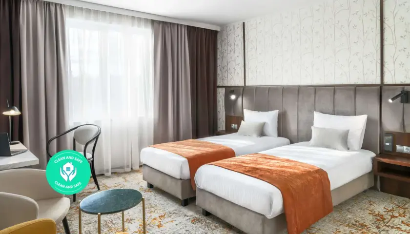 Pokój hotelowy z dwoma łóżkami, oknem i miejscem do pracy. Dowiedz się, ile kosztuje nocleg w Krakowie, szukając komfortowych opcji.