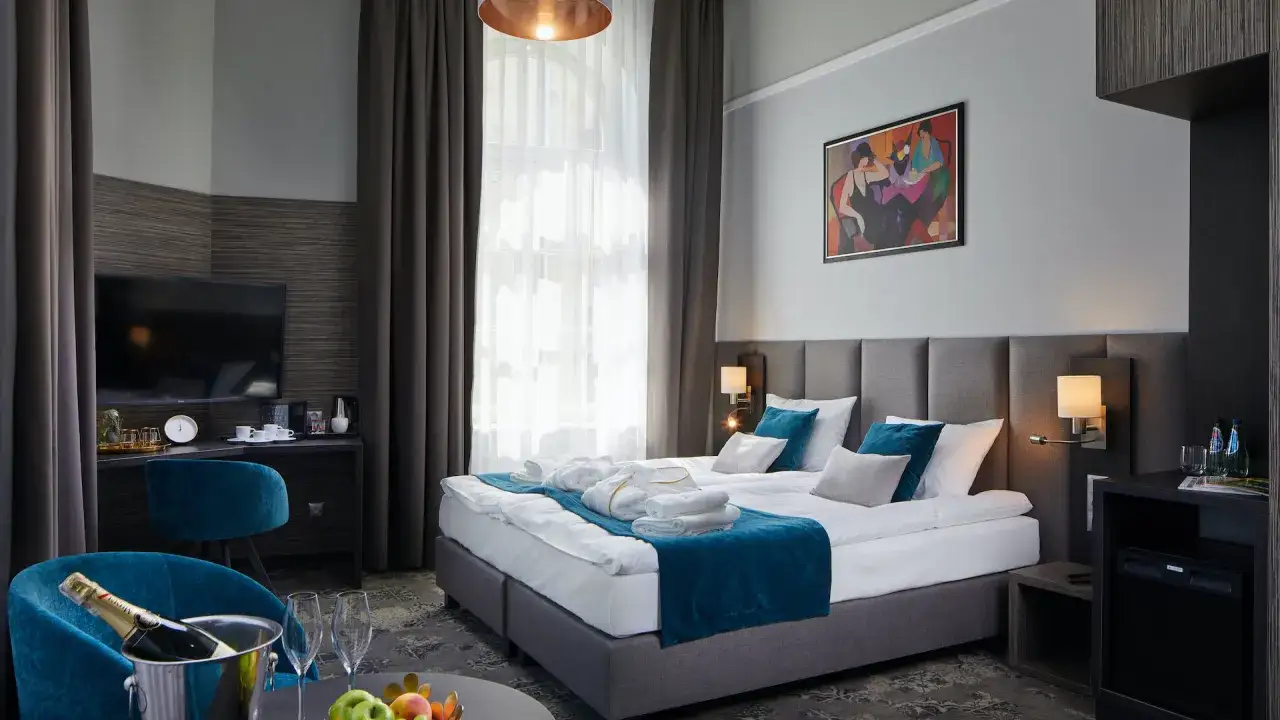 Elegancki pokój hotelowy z podwójnym łóżkiem, szlafrokami i butelką szampana. Zastanawiasz się, ile kosztuje nocleg w Krakowie?